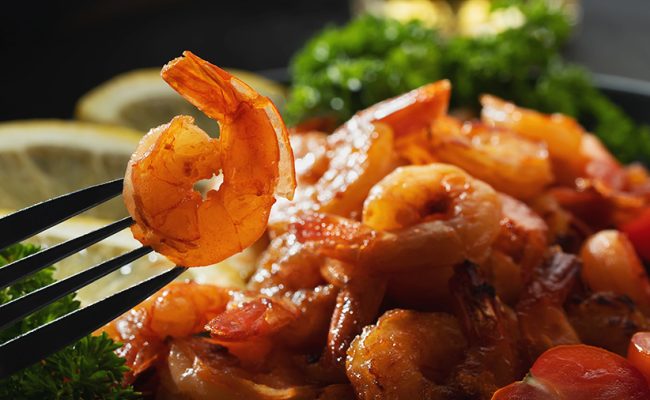 Fried shrimp on a fork close-up on a background of shrimp and greens on a plate.